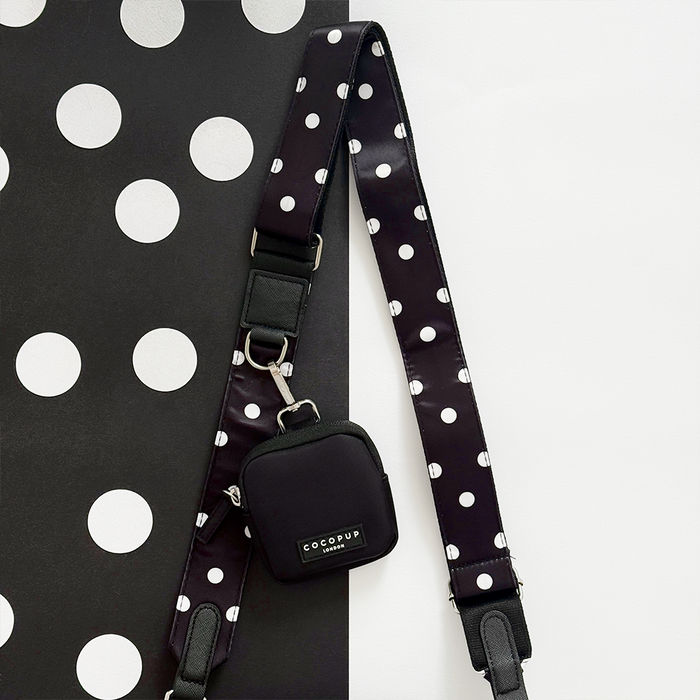 Black crossbody bag with white polka dots and matching treat pouch on a polka dot background.
