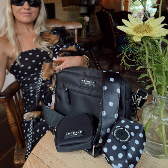 Woman in polka dot dress holding dog with Cocopup London polka dot poop bag holder and matching accessories on table.