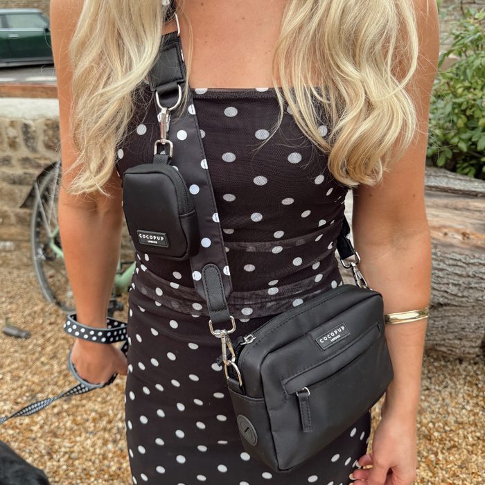 Woman outdoors in a polka dot dress with Cocopup London polka dot bag strap and beige dog walking bag, holding a leash.