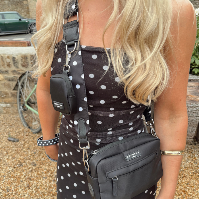 Woman with a polka dot Cocopup London dog walking bag, wearing a matching dress, standing beside a bicycle outdoors.