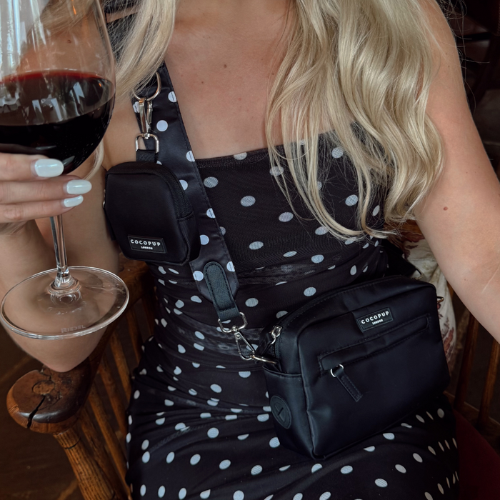 Woman in a polka dot dress holds red wine, wearing two spotted Cocopup London dog walking bags.