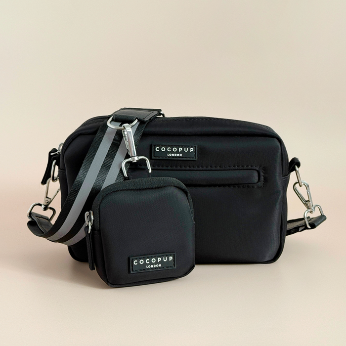 Reflective black dog walking bag with striped strap and treat pouch, displayed on a beige background.