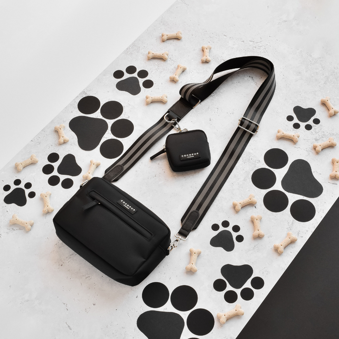 Reflective black Cocopup London dog walking bag and treat pouch on a paw print and bone pattern surface.