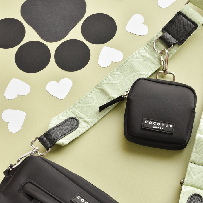 Cocopup London sage green dog walking bag with heart print, shown on a green surface with paw prints and hearts.