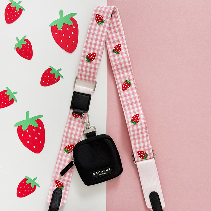 Pink dog walking bag with strawberry pattern, matching treat pouch, and poop bag dispenser, all with strawberry details.