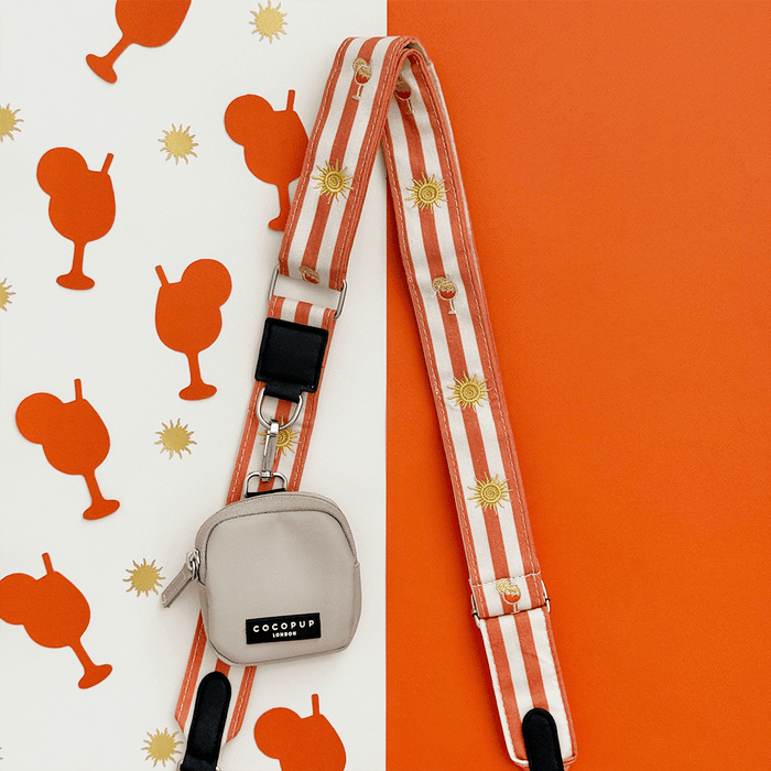 A orange and beige stripe bag strap, with embroidered drink and sun graphics. Attached is a small beige pouch for dog treats.