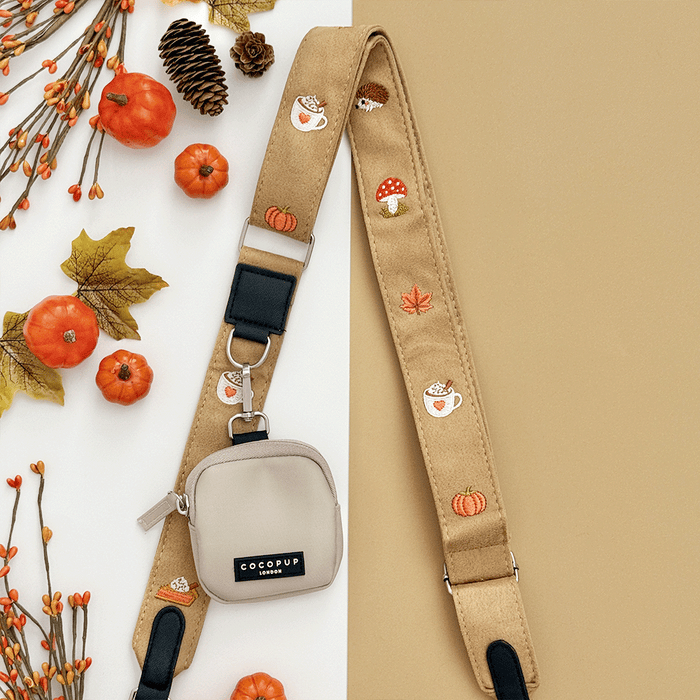 Brown bag strap, with attached treat pouch, with autumnal-themed embroidery of pumpkins, leaves, a coffee cup, and mushrooms.