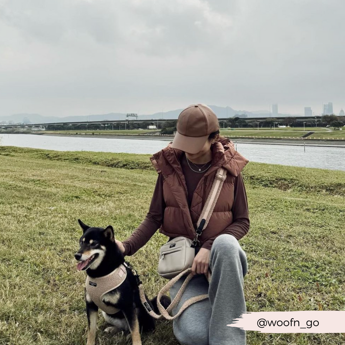 @woofn_go sits riverside, petting her Shiba Inu beside a tan Cocopup London Teddy Rupert dog walking bag.