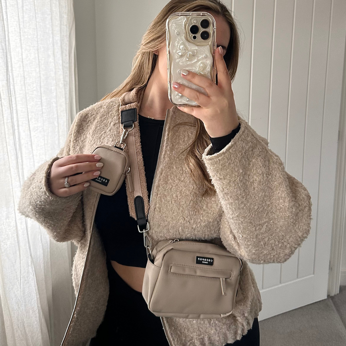 Woman in a beige jacket holds a tan Cocopup London Teddy Rupert crossbody dog walking bag in a mirror selfie.