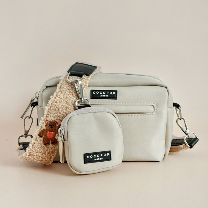 Beige Cocopup London crossbody dog walking bag with embroidered teddy, treat pouch, and attached poop bag dispenser.