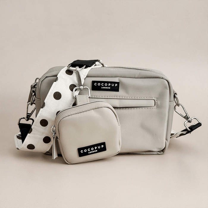 Light gray handbag with matching pouch and polka dot strap on a beige background