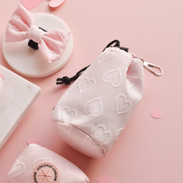 Baby pink heart-patterned Cocopup London drawstring treat pouch with matching pink bow on pastel pink background.