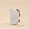 Brown tweed Cocopup London drawstring treat pouch next to three bone treats on a beige surface.