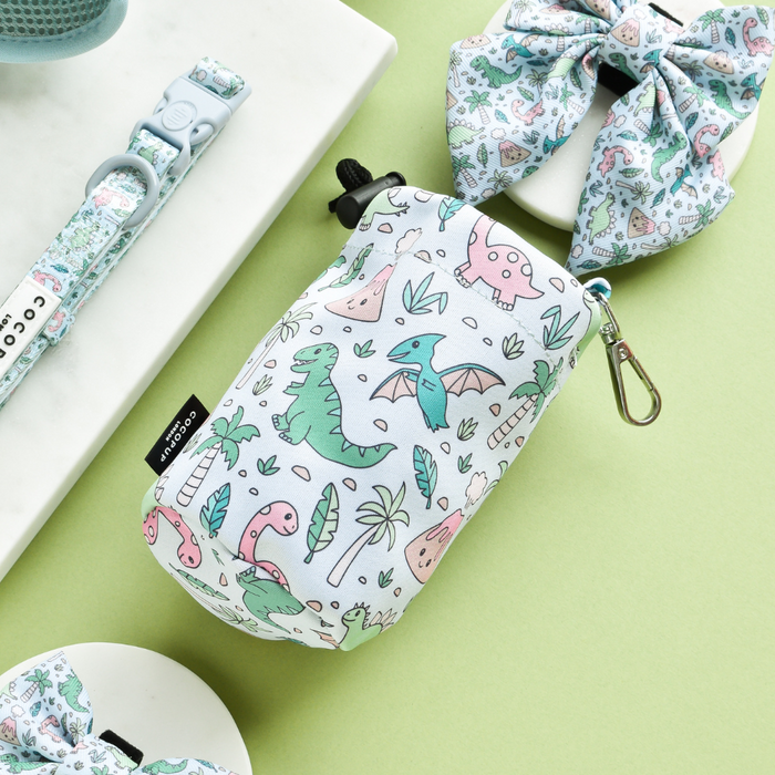 Cocopup London Dinopaws drawstring treat pouch with matching leash and bows, all on a green background.