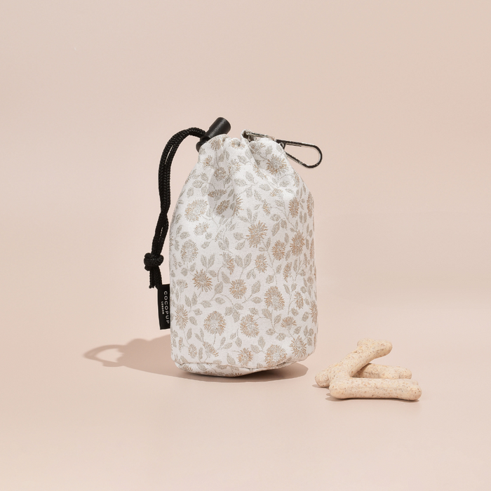 Garden Meadow print treat pouch with black drawstrings next to three bone treats on a beige background.
