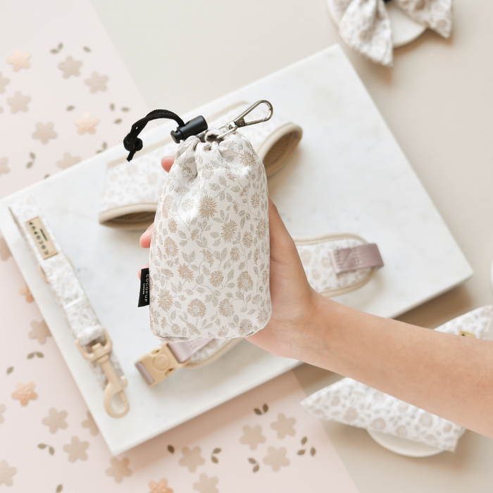 Hand holding a floral Cocopup London drawstring treat pouch, with matching floral dog accessories beside it.