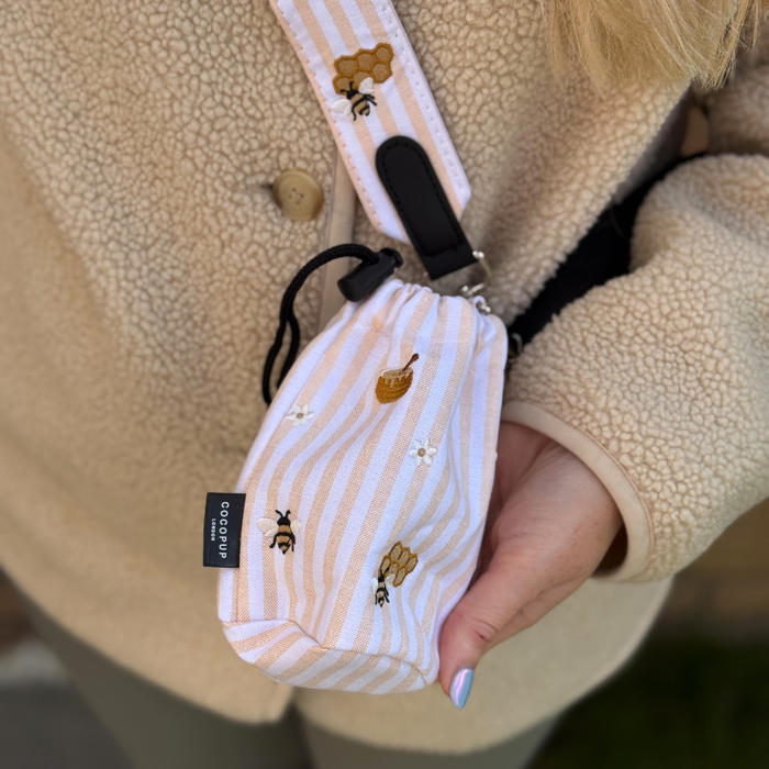 Cocopup London drawstring treat pouch in Honey Meadow, featuring a bees and honeycomb print, worn with a beige coat.