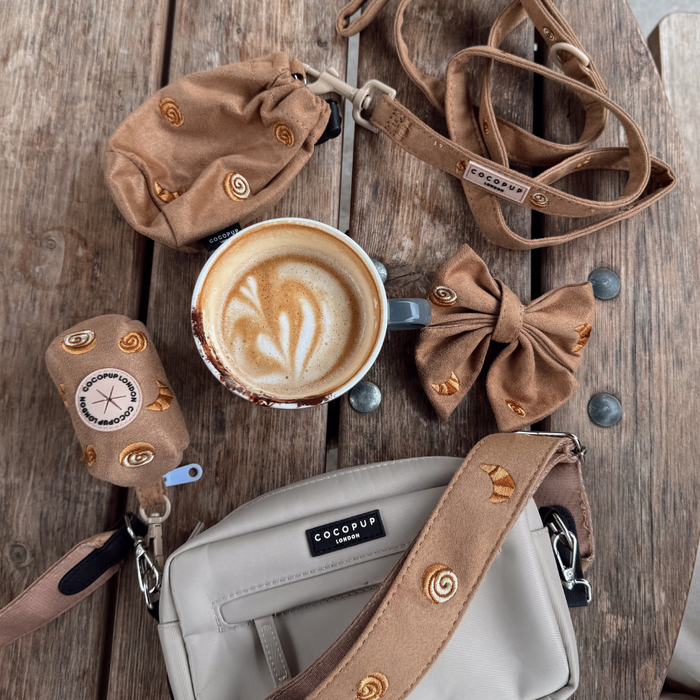 Latte in a ceramic cup on wooden table next to tan pet accessories and beige Cocopup London Pawtisserie treat pouch.