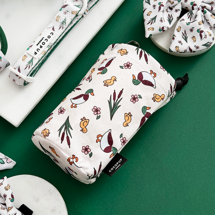 Cocopup London drawstring treat pouch in Puddle Pup pattern on green surface beside a dog collar.