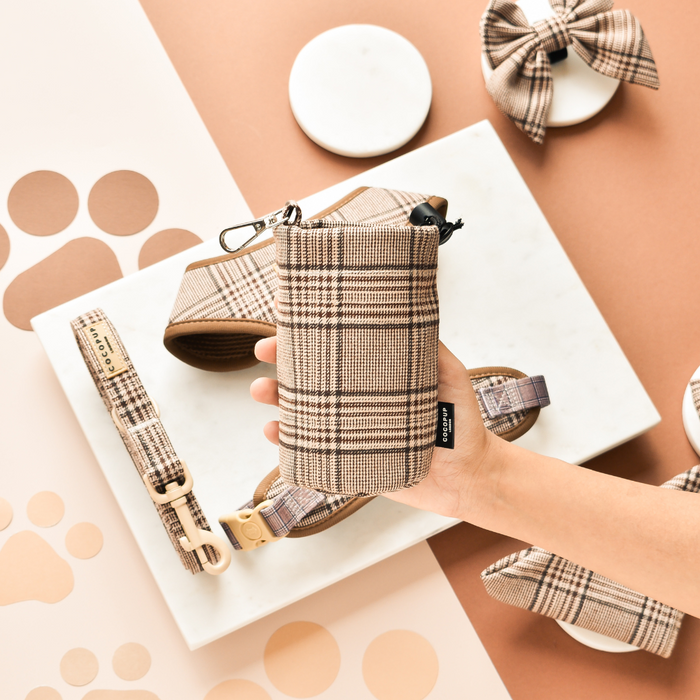 Hand holding a plaid Cocopup London treat pouch with matching pet accessories arranged nearby.