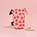Cocopup London Pupberry Fields drawstring treat pouch with plaid pattern next to bone biscuits on a pink background.