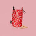 Red and pink leopard print drawstring treat pouch with two bone-shaped treats on a pink background.
