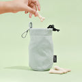 Sage tweed drawstring treat pouch from Cocopup London, filled with treats, with a hand holding a bone-shaped treat above it.