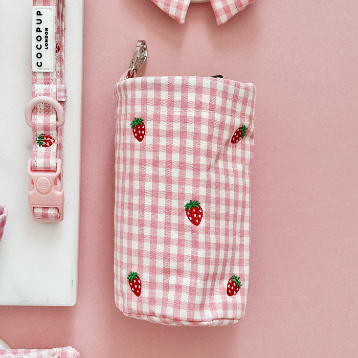 Pink Cocopup London drawstring treat pouch with strawberry print beside a matching pink and strawberry-patterned collar.