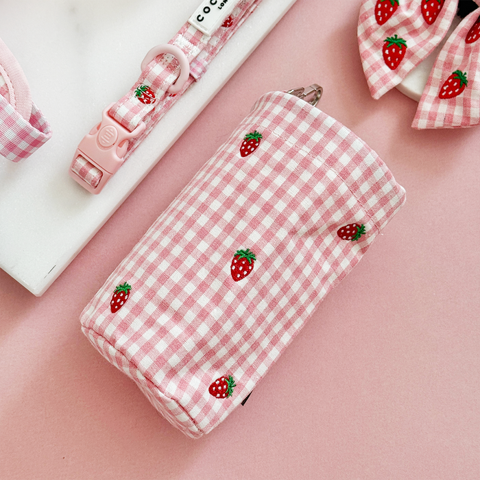 Strawberry-print drawstring treat pouch and matching dog accessories on a pink background.