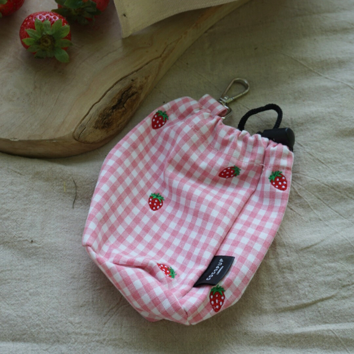 Strawberry-patterned Cocopup London drawstring treat pouch on beige fabric beside fresh strawberries and a wooden board.