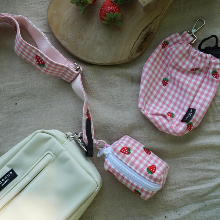 Pink gingham drawstring treat pouch with strawberry accents and matching accessories, viewed from above.
