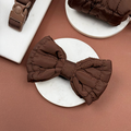 Espresso brown quilted bow tie by Cocopup London on a round white surface, set against a brown background.