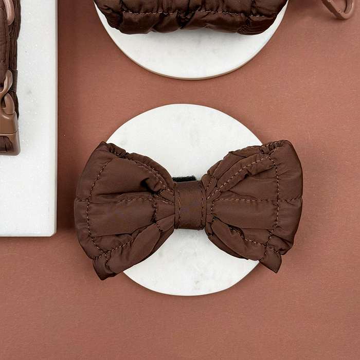 Chocolate brown quilted bow tie with a subtle sheen, displayed on a white marble surface.