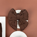 Espresso brown quilted sailor bow tie for pets displayed on a round white surface with a brown background.