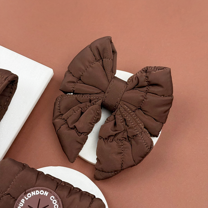 Espresso brown quilted sailor bow tie with subtle stitching, shown on a white round surface against a brown background.
