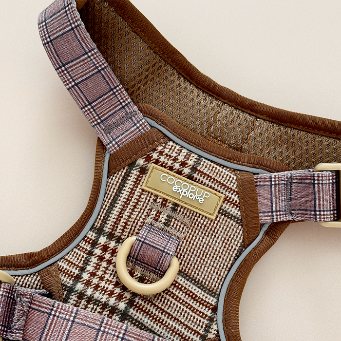 Brown plaid adjustable dog harness with mesh lining and gold logo, shown against a beige background.