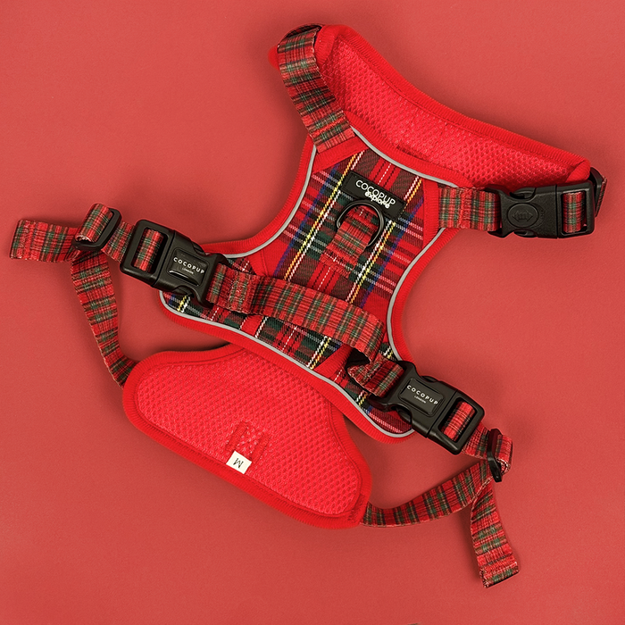 Red tartan dog harness with black buckles and reflective accents, shown against a red background.
