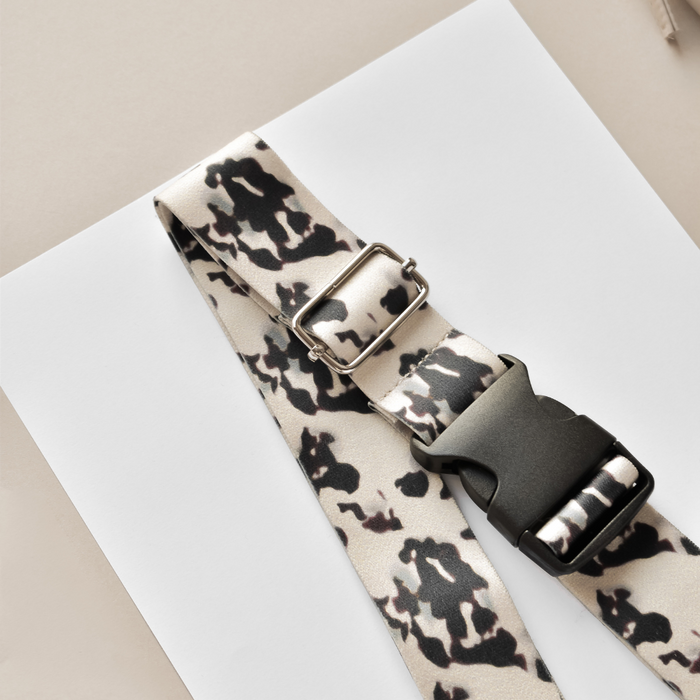 Ivory tortoiseshell-patterned Cocopup London bum bag strap with plastic buckle, laid diagonally on white paper.
