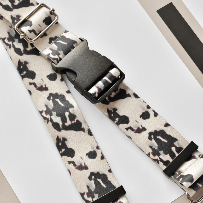 Black buckle on an ivory-patterned Cocopup London bum bag strap, displayed on white and gray paper.