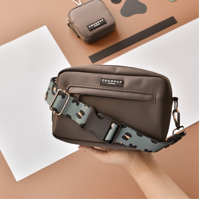 Khaki leopard Cocopup London bag strap held in hand, clipped to a brown dog walking bag against a beige background.