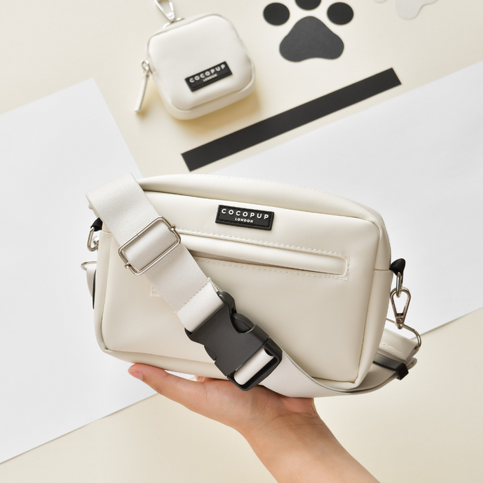Hand holding an Oyster White Cocopup London bum bag strap attached to a matching dog walking bag and small pouch.