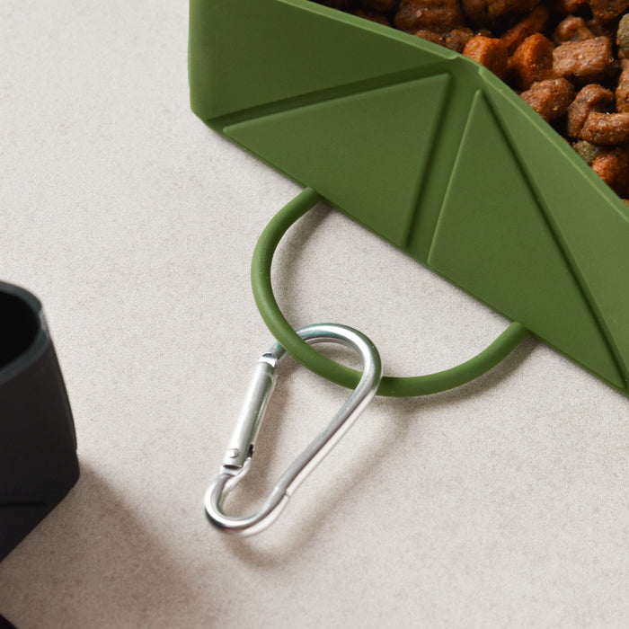 Khaki foldable travel bowl with kibble inside and a silver carabiner, shown on a light background.