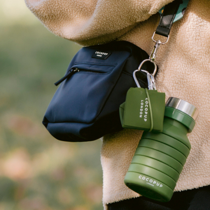 Black pouch bag with a khaki foldable travel bowl attached, worn over a beige fleece jacket.