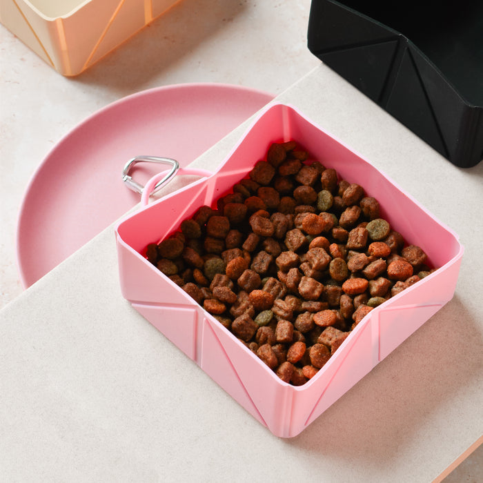 Pink Cocopup London foldable travel bowl with kibble beside a matching pink plate on a countertop.