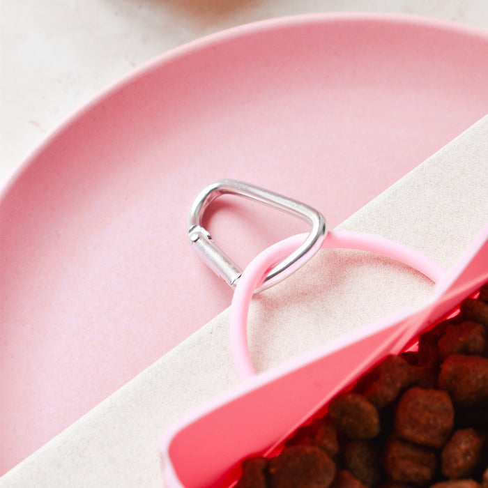 Pink Cocopup London foldable travel bowl with pet food, shown with a pink scoop featuring a silver handle.