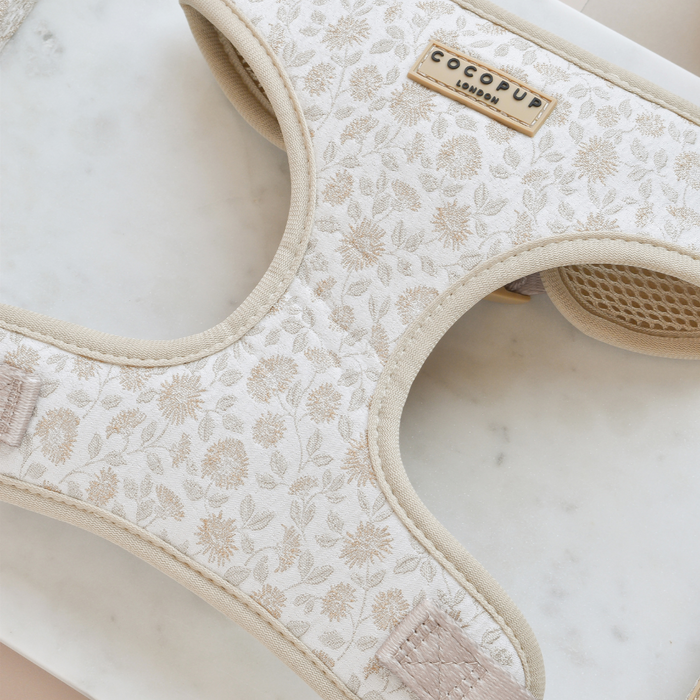 A chic and fashionable Luxe Adjustable Neck Harness – Garden Meadow by Cocopup London, featuring a white and beige embroidered floral pattern, is displayed on a marble surface.