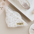 A Luxe Bandana - Garden Meadow in beige and white floral pattern, folded into a triangle, is placed on a white surface. Attached to the bandana is a gold label reading "Cocopup London." Nearby are other items from the Cocopup range with similar patterns and colors, including a Garden Meadow print pouch and part of a card.