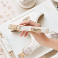 A hand holds a beige and white Luxe COLLAR - Garden Meadow by Cocopup London above matching pet accessories.