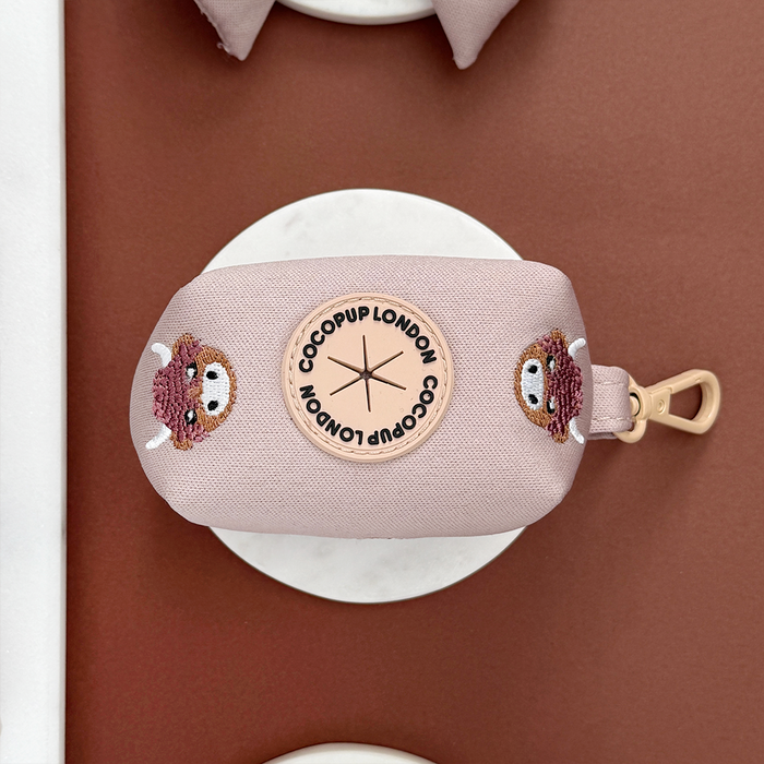 Brown Highland Cow poop bag holder with Cocopup London round logo patch and a gold clip, on a brown and white background.