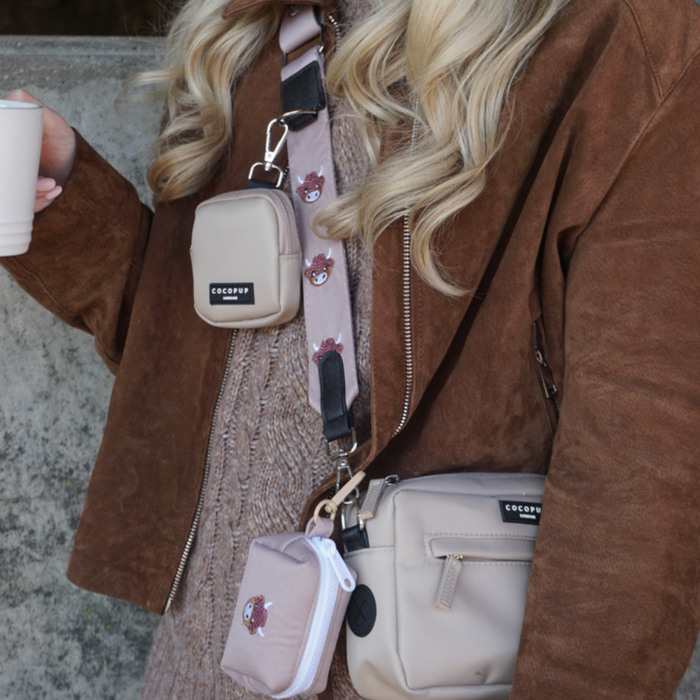 Woman in a brown jacket carrying a Cocopup London crossbody dog walking bag with a cow print strap.